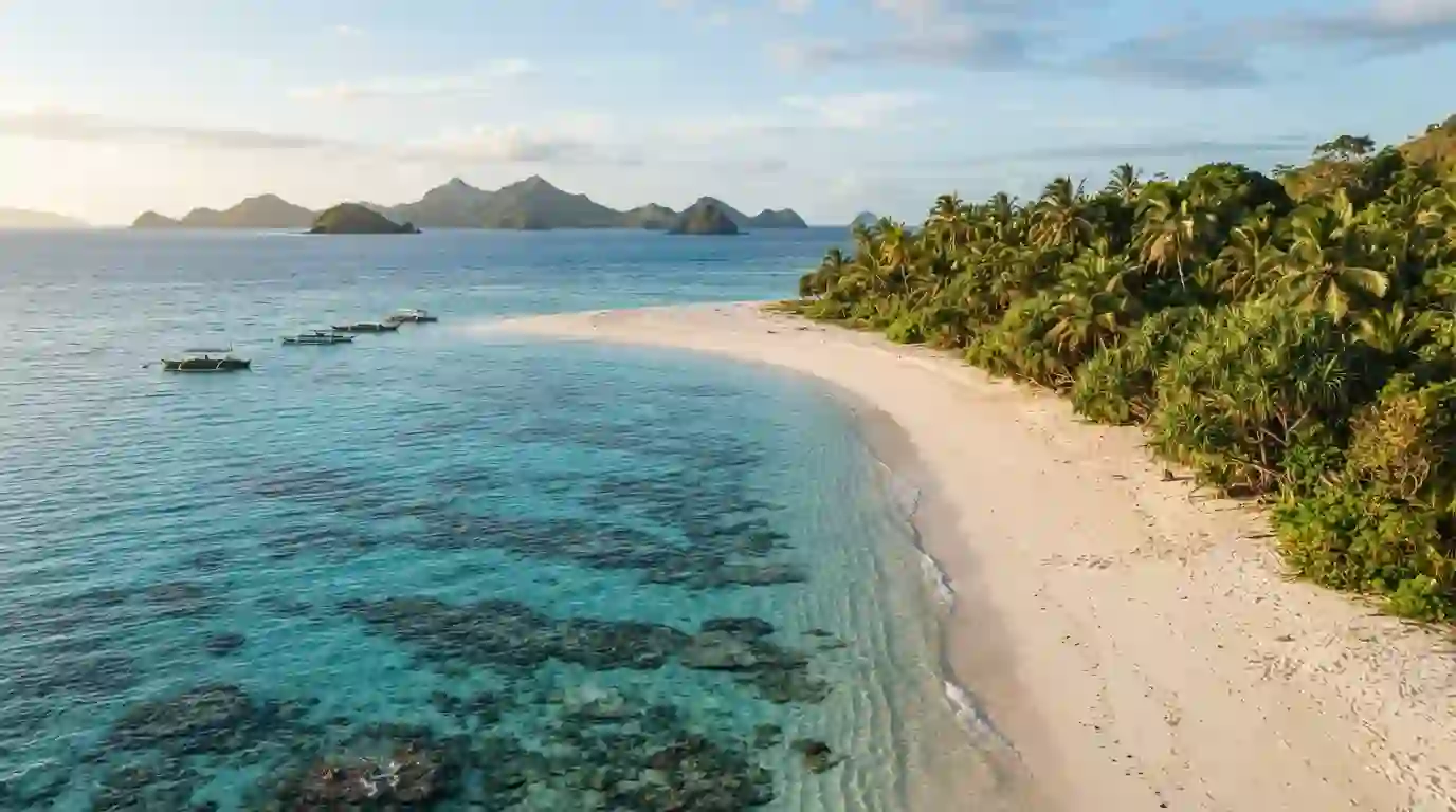Tropical Fijian island with a white-sand beach, turquoise water, palm trees, and distant islands